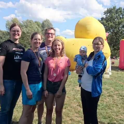 Sechsköpfige Gruppe von Menschen mit Medaillen vor einem bunten Hüpfburg und einem großen gelben Luftballon.
