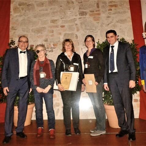 Gruppenbild von fünf Personen, die eine Zeremonie in historischen Kostümen und Ansteckern feiern. Hintergrund mit Pflanzen.