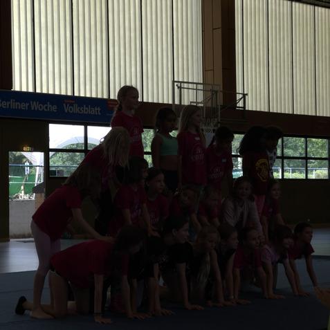 Gruppe von M&auml;dchen in pinken T-Shirts, die auf einer Gymnastikmatte eine Menschenpyramide bilden.