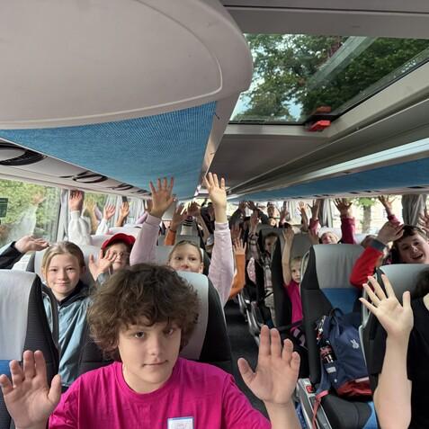 Businnere des Schul-Ausflugs mit Kindern, die fr&ouml;hlich die H&auml;nde heben, in einem bunten Reisebus.
