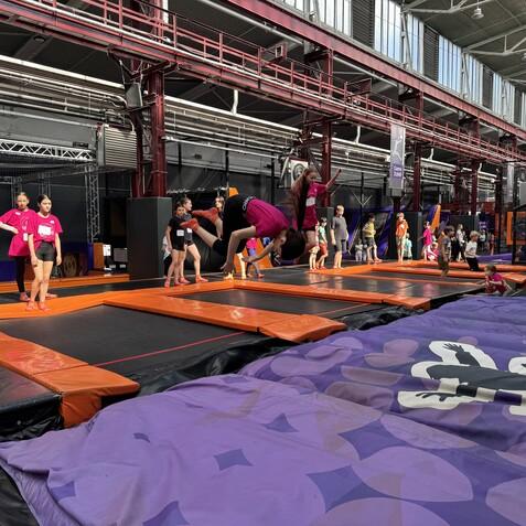 Kinder und Jugendliche in bunten T-Shirts springen auf Trampolinen in einer Indoor-Trampolinhalle.