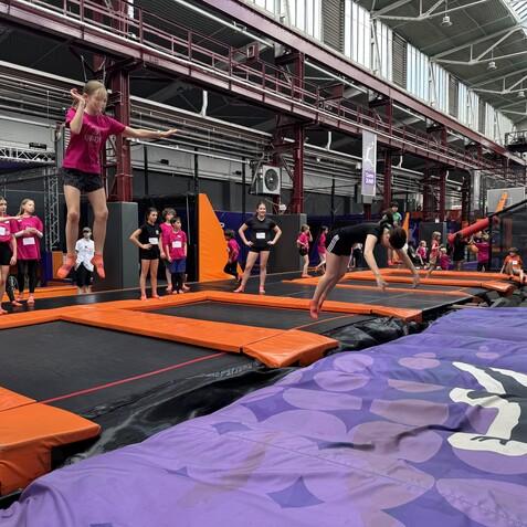 Kinder springen auf Trampolinen in einer Trampolinhalle mit orangefarbenen und schwarzen Belägen.