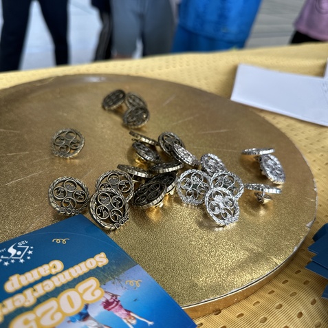 Silberne Medaillen und ein Informationsblatt &uuml;ber einen Sportcamp-Event liegen auf einem goldenen Tablett.