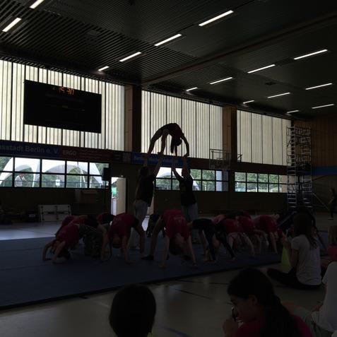 Gruppe Kinder in pinken T-Shirts f&uuml;hrt akrobatische &Uuml;bungen auf Matte in einer Sporthalle durch.