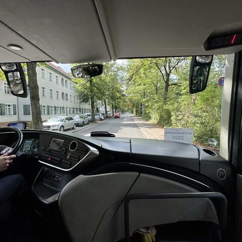 Fahrerblick aus einem Bus auf eine gr&uuml;ne Stra&szlig;e mit parkenden Autos und H&auml;usern aus der Sicht des Fahrers.