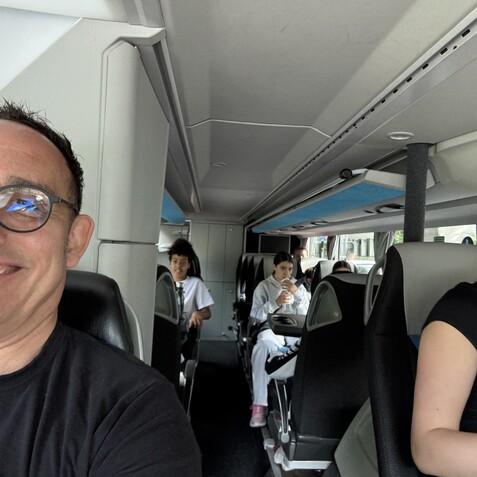 Selbstportr&auml;t eines Mannes am Steuer eines Busses mit Jugendlichen im Hintergrund, die entspannt sitzen.