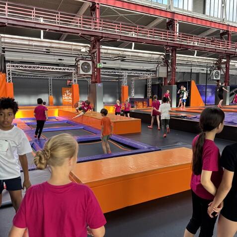 Gruppenszene in einer Trampolinhalle mit Kindern in bunten Shirts, die auf Trampolinen spielen und herumgehen.