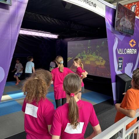 Gruppe von Kindern steht vor einem Bildschirm in der VALOARENA, die interaktive Spiele bietet.