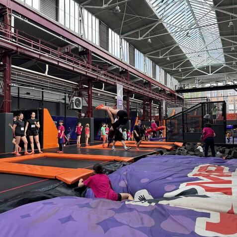 Kinder und Jugendliche springen auf einer Trampolinfl&auml;che in einer Halle mit bunten W&auml;nden und weichen Schaumstoffbl&ouml;cken.