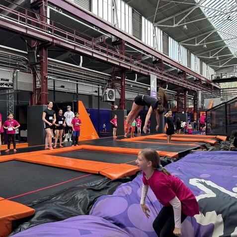 Gruppentrennveranstaltung in einer Trampolinhalle mit Kindern, die auf Trampolinen springen und zuschauen.