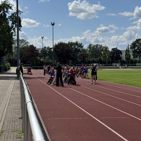 Gruppe von Kindern und Erwachsenen beim Training auf einer roten Laufbahn unter blauem Himmel.