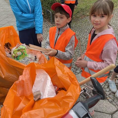 Gruppe von Kindern in Warnwesten mit M&uuml;llsack, sammeln Abfall bei einer Umweltschutzaktion. Einige halten M&uuml;llgegenst&auml;nde.
