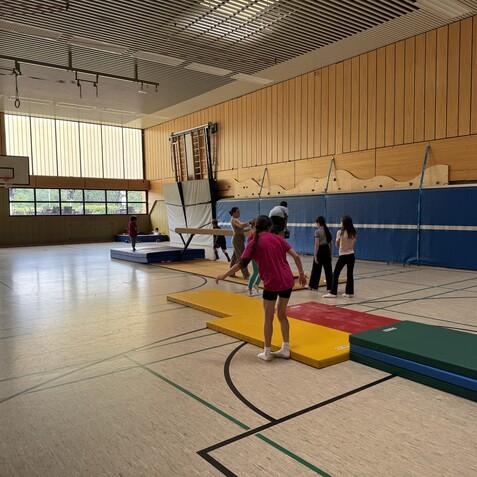 Kinder trainieren in einer Turnhalle auf verschiedenen Matten und Ger&auml;ten unter Tageslicht.