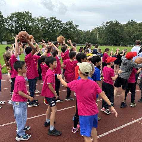 Gruppenspiel mit Kindern in pinken T-Shirts, die Basketballb&auml;lle auf einem Sportplatz werfen und fangen.