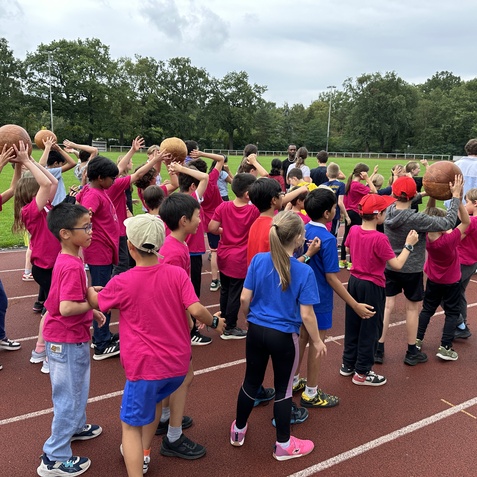 Gruppe von Kindern in pinken T-Shirts, die Basketballb&auml;lle auf einem Sportplatz halten.