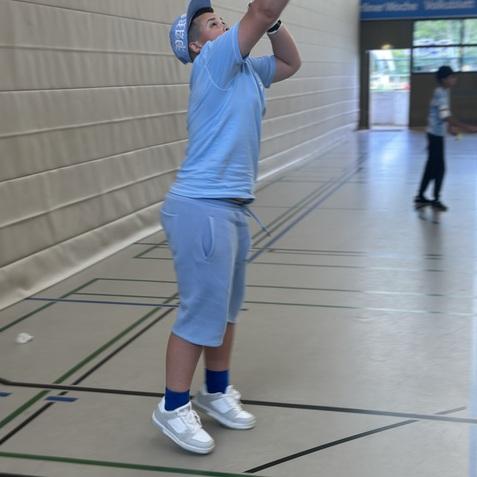 Ein Junge in blauer Sportkleidung schlägt mit einem Schläger einen Ball in einer Sporthalle.