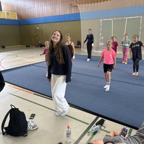 Gruppen von Kindern und Jugendlichen trainieren in einer Sporthalle, eine Person lächelt in der Mitte der Szene.