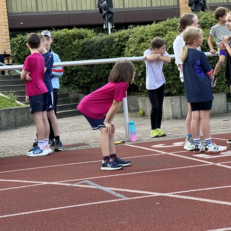 Gruppe von Kindern auf einer Laufbahn, einige warten, andere unterhalten sich vor einem Wettlauf.