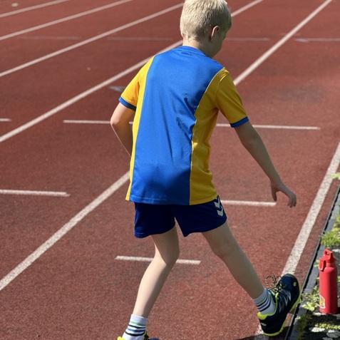 Ein Junge in gelb-blauem Sportoutfit steht auf einer Laufbahn und bereitet sich auf den nächsten Sprint vor.