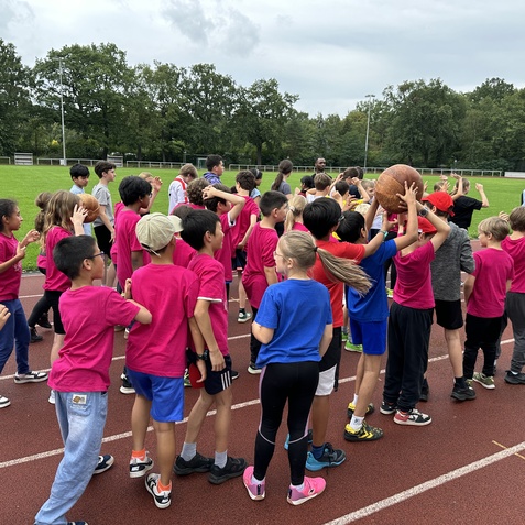 Gruppierung von Kindern in sportlichen T-Shirts, die auf einer Laufbahn stehen und einen Basketball halten.