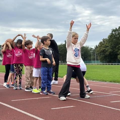 Gruppe von Kindern auf einer Laufbahn, bereit f&uuml;r einen Wettkampf, einige mit erhobenen H&auml;nden.