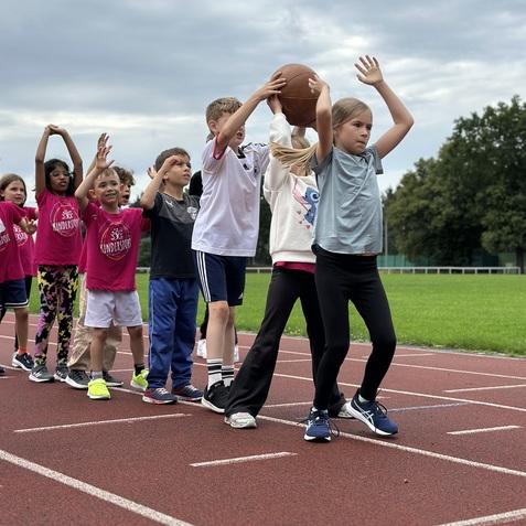Gruppe von Kindern auf einer Laufbahn, die gemeinsam mit einem Basketball &Uuml;bungen durchf&uuml;hren.