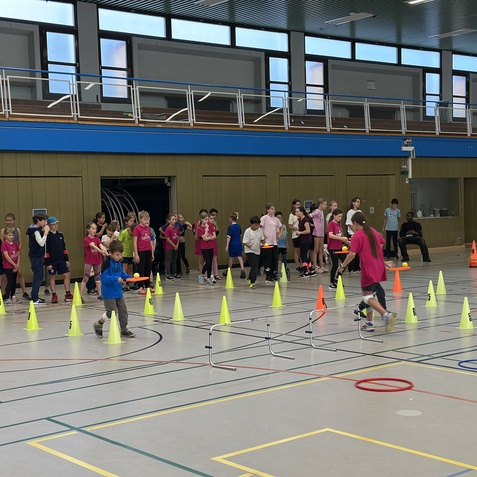 Kinder in einer Sporthalle mit Sportausr&uuml;stung und H&uuml;tchen