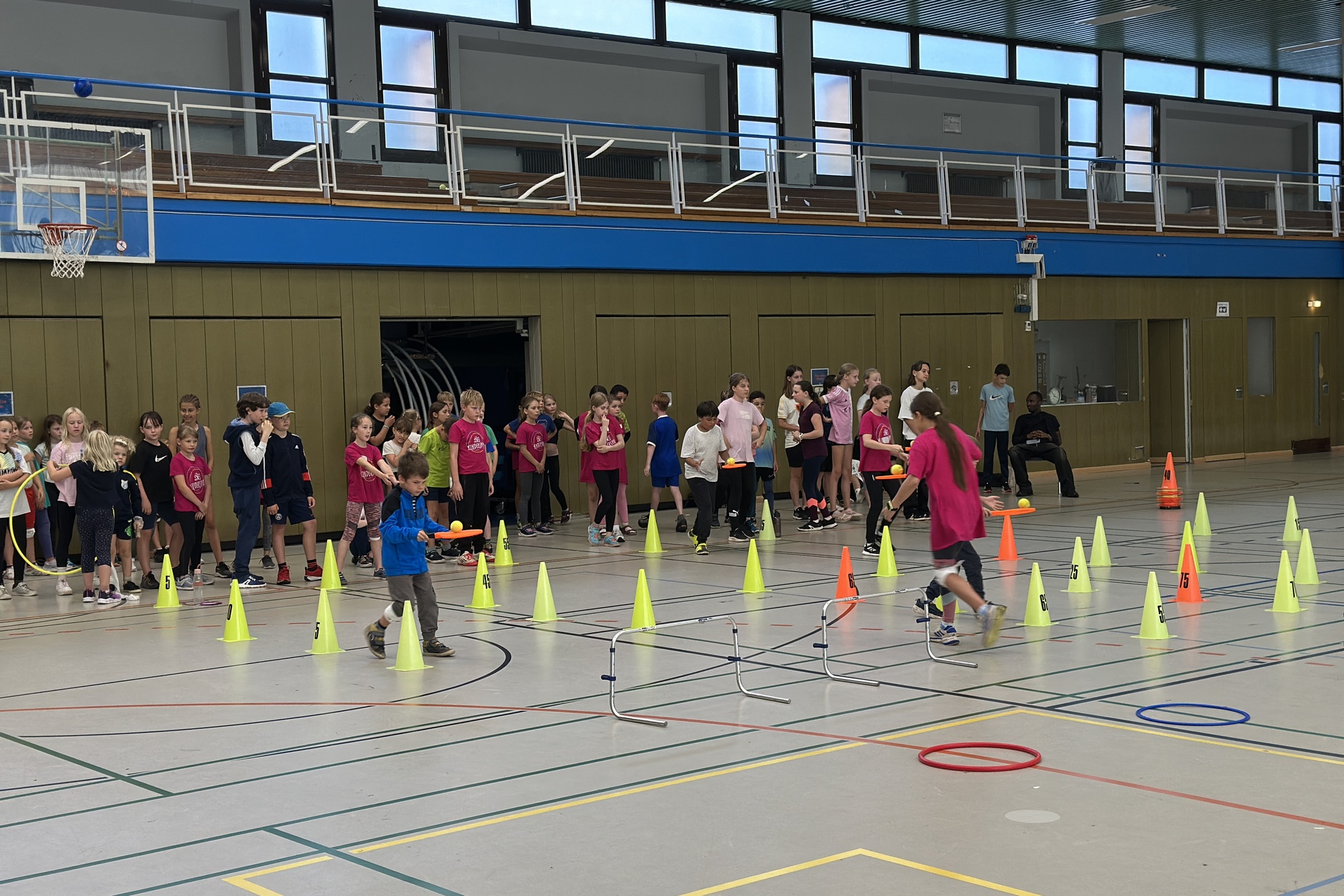 Kinder in einer Sporthalle mit Sportausr&uuml;stung und H&uuml;tchen