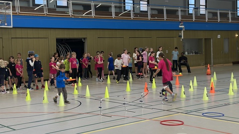 Kinder in einer Sporthalle mit Sportausrüstung und Hütchen