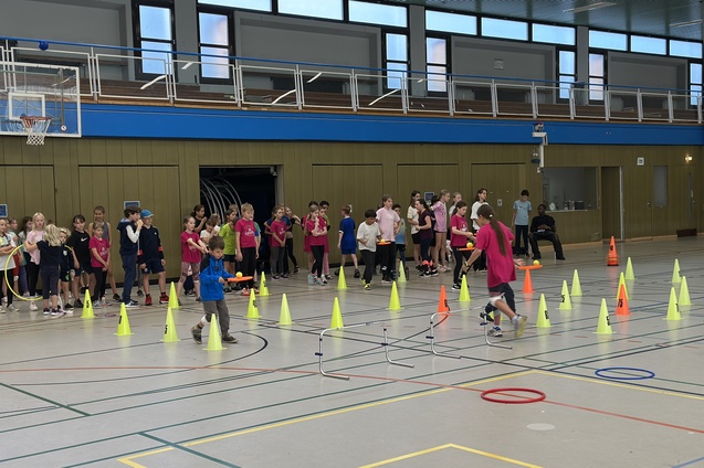 Kinder in einer Sporthalle mit Sportausr&uuml;stung und H&uuml;tchen