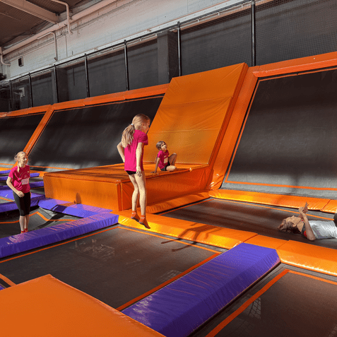 Kinder springen und spielen auf einer bunten Trampolinanlage mit orangefarbenen und lila Matten.
