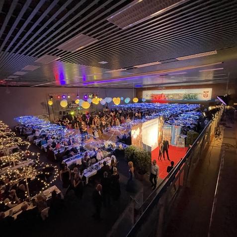 Belebte Veranstaltungshalle mit festlich dekorierten Tischen und stimmungsvoller Beleuchtung. G&auml;ste tanzen und feiern.