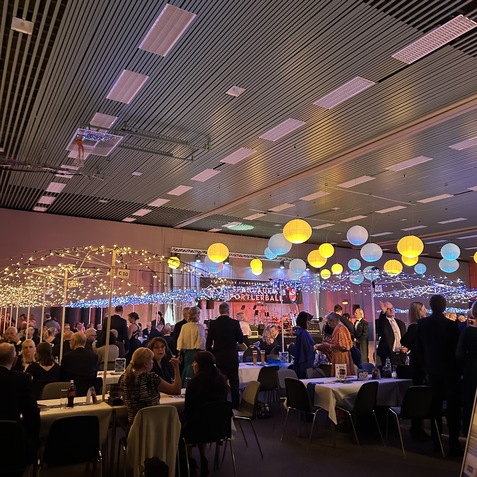 Elegante Veranstaltungshalle mit festlich gedeckten Tischen, Lichtern und Gästen in formeller Kleidung.