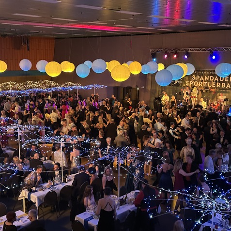 Voller Festsaal beim Spandauer Sportlerball mit tanzenden Gästen und festlicher Beleuchtung. Bühne im Hintergrund sichtbar.