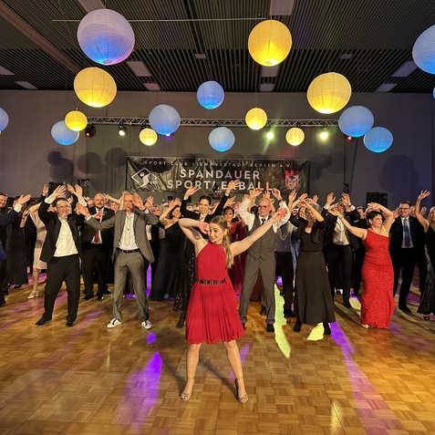 Tanzende Menschen in eleganter Kleidung, umgeben von bunten Laternen, auf einem festlichen Ball in einer Halle.