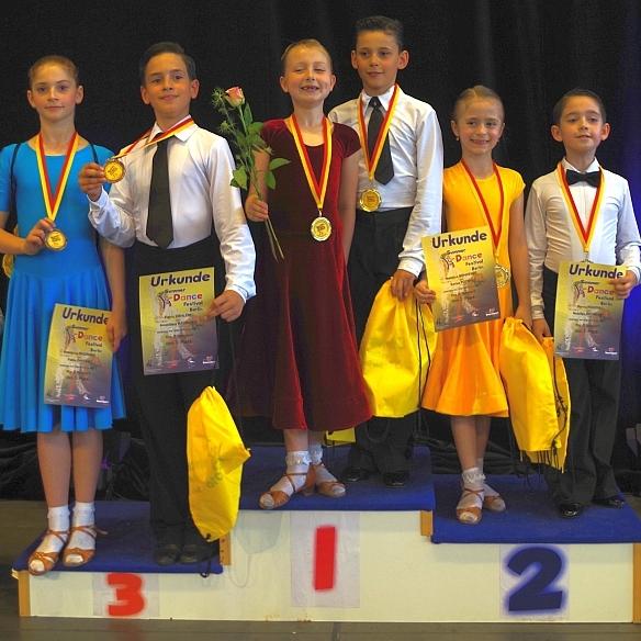 Sechs Kinder stehen auf dem Podest nach einem Tanzwettbewerb, tragen Medaillen und halten Urkunden und Blumen.