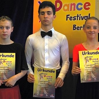 Fünf Tänzer in eleganter Kleidung halten Urkunden des Dance Festivals in Berlin. Hintergrund mit festlicher Dekoration.