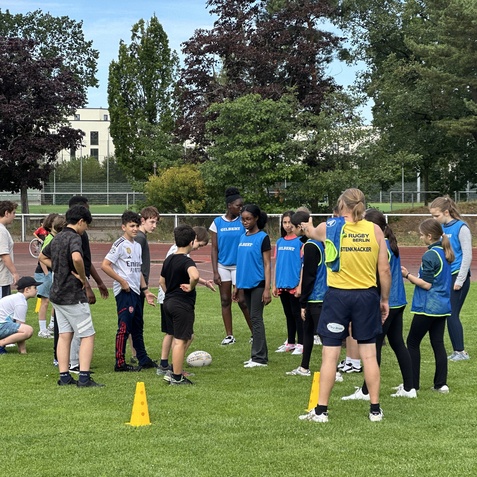 Gruppe von Kindern und Jugendlichen in Trainingsanz&uuml;gen bei einem Rugby-Training auf einem Rasenplatz.