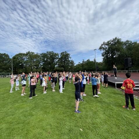 Gruppentraining im Freien mit zahlreichen Teilnehmern, die Übungen auf einem Sportplatz ausführen.