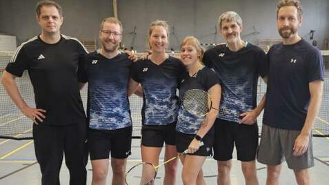 Gruppe von sechs Badmintonspielern in Sportkleidung, lächelnd, mit Schlägern, auf einem Badmintonplatz.