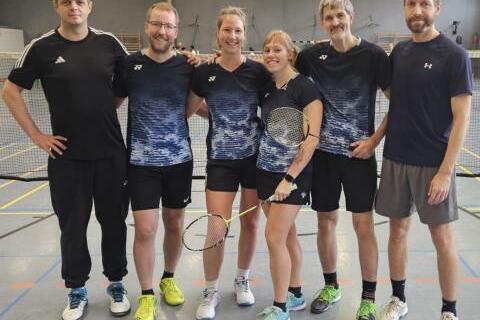 Gruppe von sechs Badmintonspielern in Sportkleidung, l&auml;chelnd, mit Schl&auml;gern, auf einem Badmintonplatz.