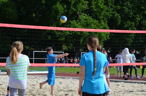 Kinder spielen Beachvolleyball auf einem Sandplatz, w&auml;hrend ein Ball &uuml;ber das Netz fliegt.