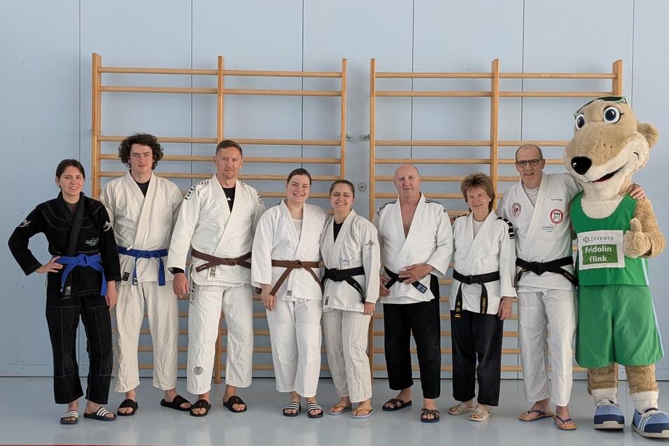 Gruppe von acht Personen in Judokleidung, stehend vor einer Kletterwand, daneben ein Maskottchen in Sportkleidung.
