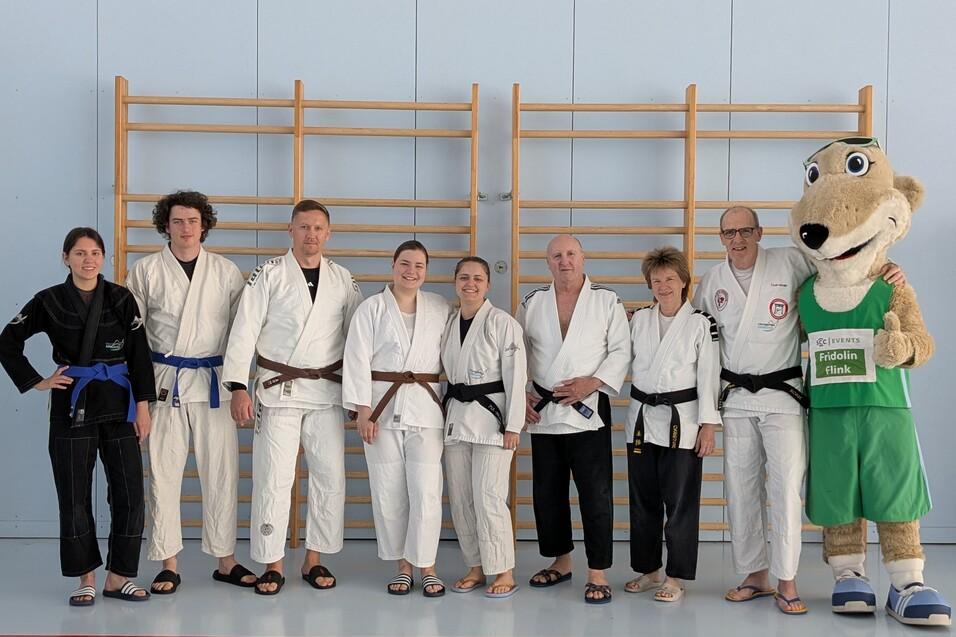 Gruppe von acht Personen in Judokleidung, stehend vor einer Kletterwand, daneben ein Maskottchen in Sportkleidung.