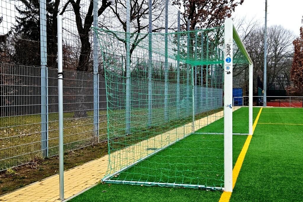 Fußballtor mit grünem Netz und Kunststoffrahmen auf einem Kunstrasenplatz, umgeben von einem Zaun.