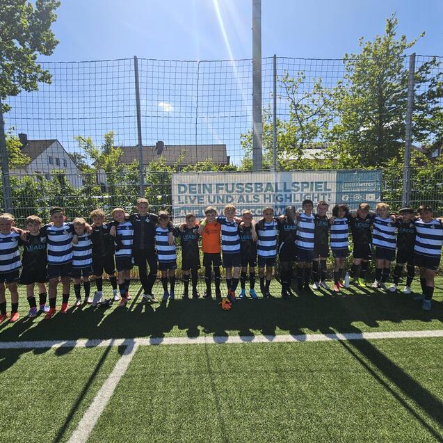 GruppennFoto von Jungen in Fu&szlig;balltrikots auf einem Kunstrasenplatz, umgeben von einem netz eingez&auml;unten Bereich.