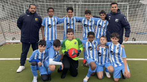Gruppenselfie einer Fußballmannschaft mit 11 Kindern und zwei Trainern vor einem Tor. Alle tragen gestreifte Trikots.