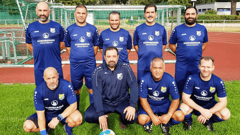 Gruppenfoto von acht Fußballspielern in blauen Trikots mit einem Ball auf einem Sportplatz vor einem Tor.