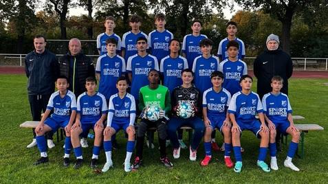 Mannschaftsfoto einer Fußball-Jugendmannschaft in blauen Trikots, Gruppierung auf einer Wiese mit Trainer und Betreuern.