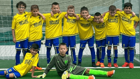 Gruppe von zehn jugendlichen Fußballspielern in gelben Trikots, pose vor einem Tor auf einem Fußballfeld.